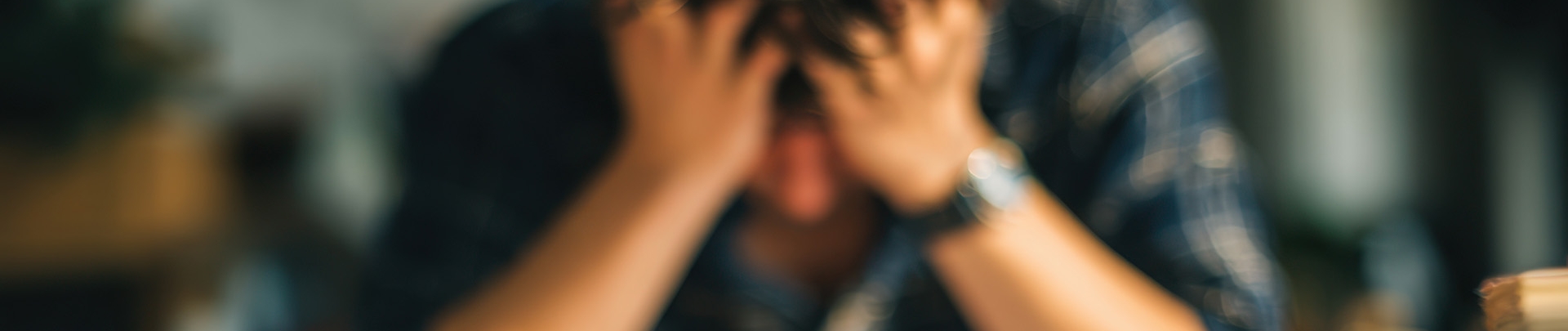 stress; man zit met handen op zijn voorhoogd achter zijn bureau
