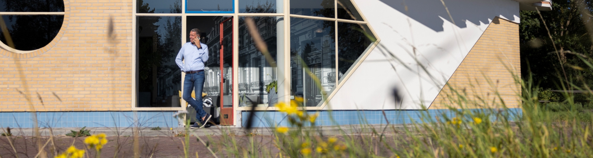 Leen Winter telefonisch in gesprek leunend tegen het pand van zijn kantoor aan